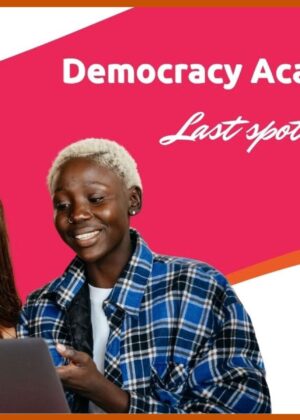 The photos of two young women working together on a laptop in an engaged manner, with the hot pink and orange colors of the academy behind them and the words "Democracy Academy 2026" and "Last spots available" superimposed on the right side.